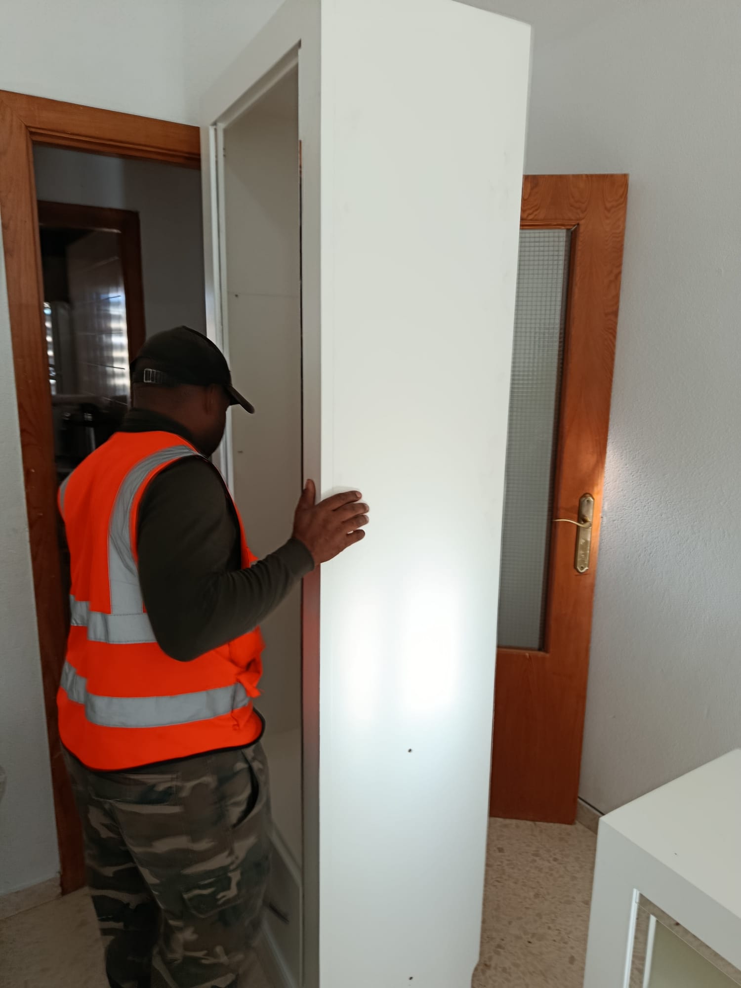 Operario moviendo un armario alto blanco por el pasillo de una vivienda